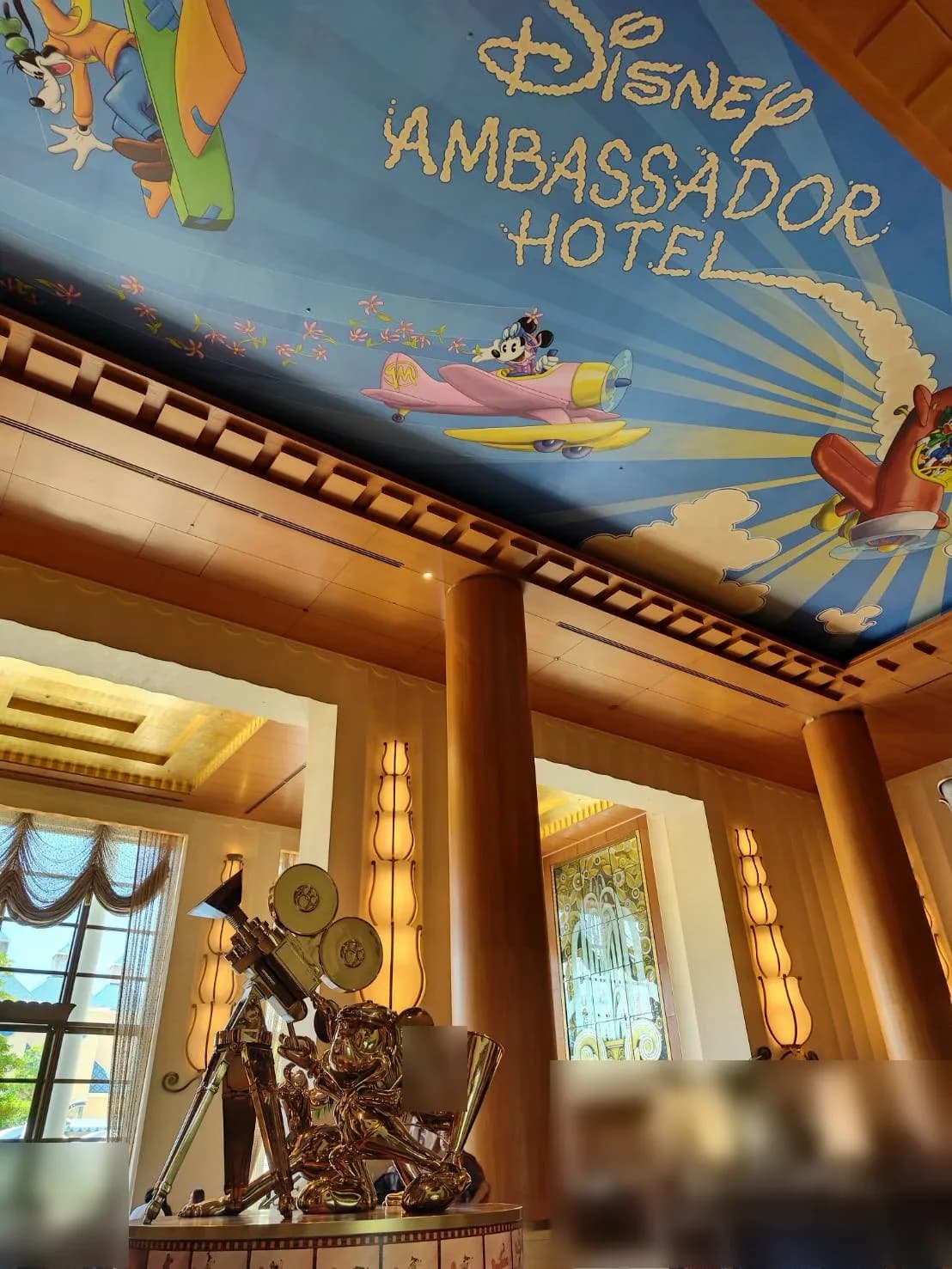 ミッキーの像の近くから見上げたロビー。天井画に DISNEY AMBASSADOR HOTEL の文字と飛行機に乗ったキャラクター