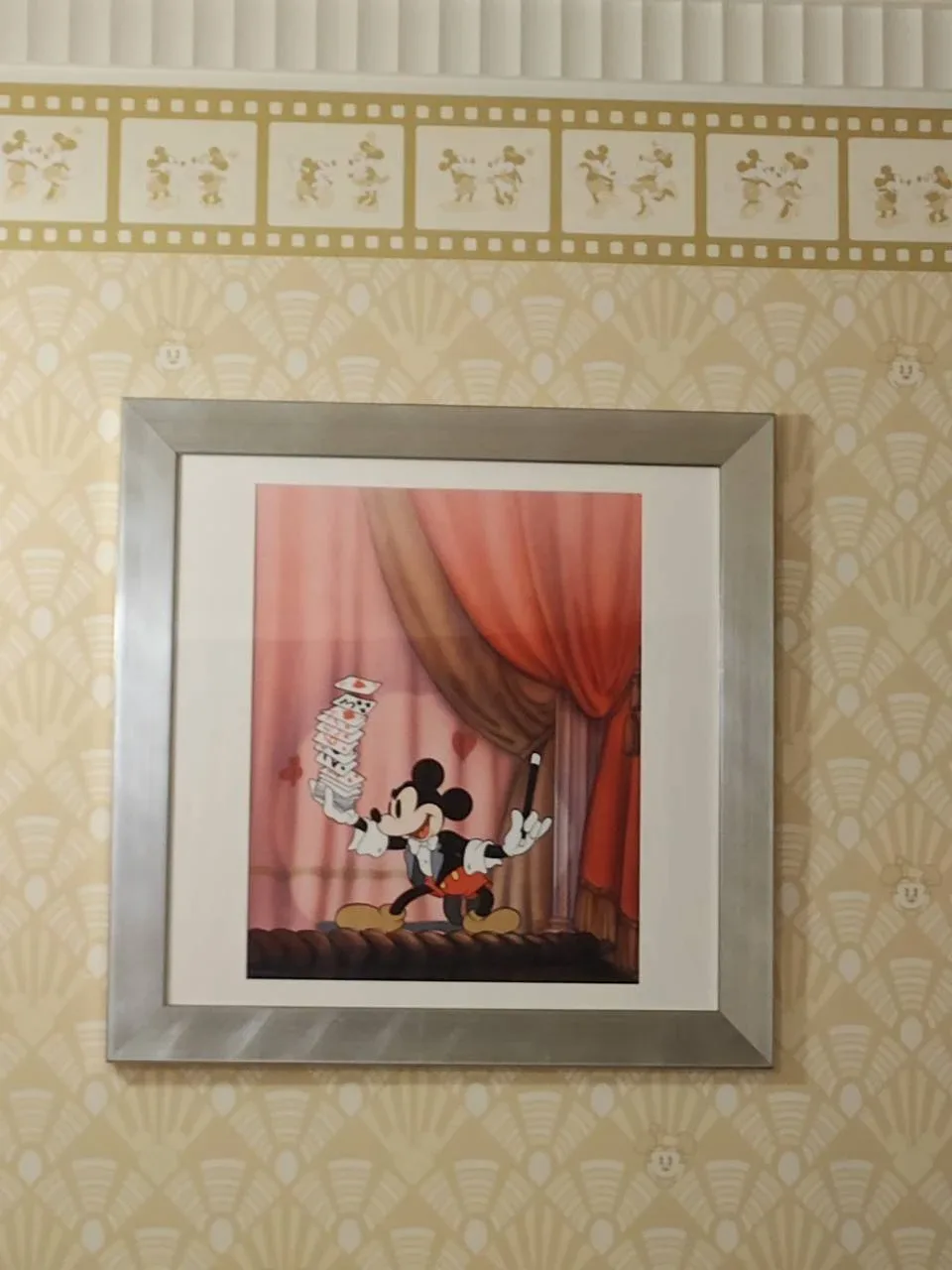 客室に飾られた額入りの絵。赤い幕の舞台でトランプを積み上げる手品師のミッキー